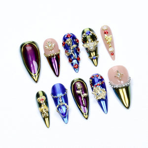 A set of ten stiletto-shaped press-on nails featuring metallic purple, blue, and gold finishes. The designs include gold rose emblems, red rhinestones, clear crystals, and star-shaped charms on a mix of solid and nude-base nails.