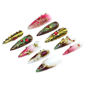 A set of ten stiletto-shaped press-on nails featuring various designs including red, green, and white gradients, gold metallic filigree, star accents, small pearls, and embedded red rhinestones arranged in a scattered pattern.