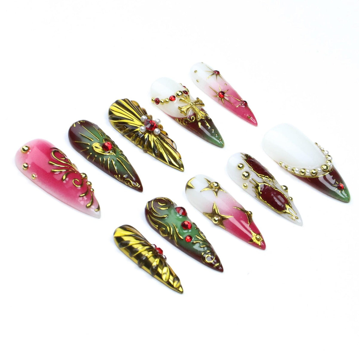 A set of ten stiletto-shaped press-on nails featuring a variety of designs including red and white gradients, metallic gold accents, embedded red rhinestones, small white pearls, and gold cross charms arranged on a plain white surface.