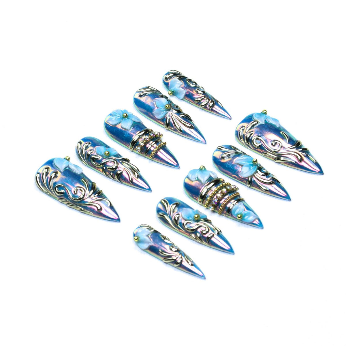 A set of ten stiletto-shaped press-on nails featuring an iridescent blue finish, raised silver filigree scrollwork, small light blue floral accents, and select nails adorned with horizontal bands of embedded clear rhinestones and gold beads.