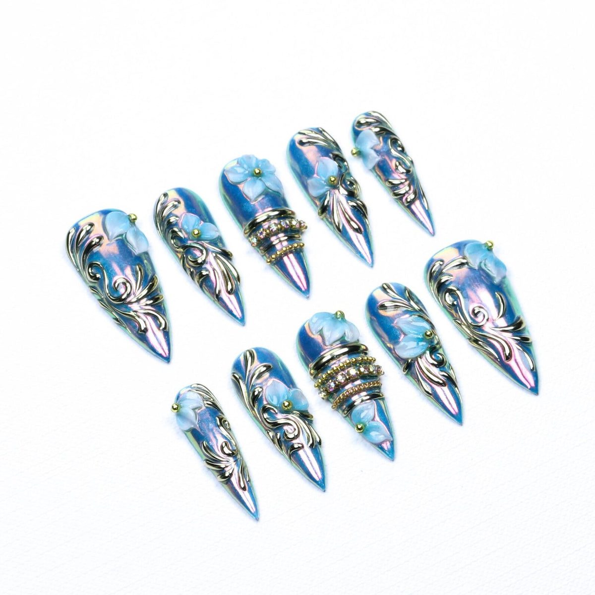 A set of ten stiletto-shaped press-on nails featuring an iridescent blue finish, silver filigree scrollwork, raised light blue floral accents, and small gold beads. Some nails include horizontal bands of clear rhinestones.