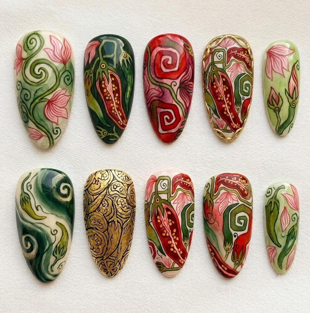 A set of ten almond-shaped press-on nails featuring hand-painted designs. The patterns include red chili peppers, swirling green vines, pink floral motifs, and one nail with a textured gold metallic finish, all arranged in two rows.