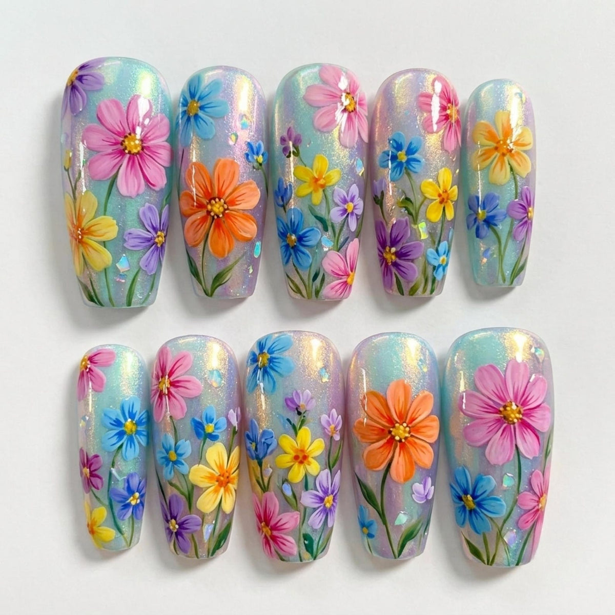 A set of ten press-on nails featuring a shimmering, iridescent light blue base. Each nail is decorated with hand-painted floral designs in vibrant shades of pink, orange, yellow, purple, and blue, accented with small green stems.