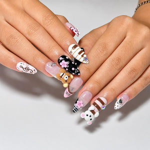 Ten pink, black, brown and white almond press on nails with 3D teddy bear charms, flowers, music notes, polka dots, stripes, pearls and rhinestones on a white background.