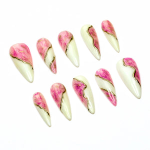 A set of ten stiletto-shaped press-on nails featuring a split design. One side is a creamy off-white, while the other side displays a vibrant pink marble pattern. A thin, metallic gold line separates the two sections on each nail.