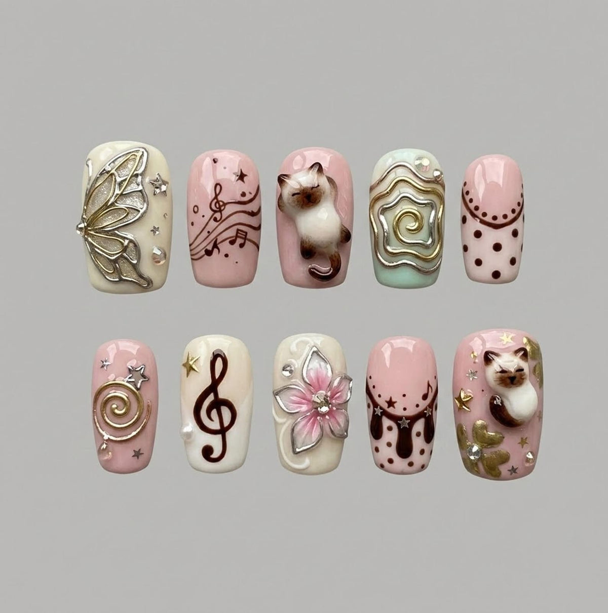 A set of ten press-on nails featuring various designs including a 3D butterfly, musical notes, a 3D cat figure, swirling gold lines, polka dots, a 3D pink flower, and small star accents in shades of cream, soft pink, and brown.