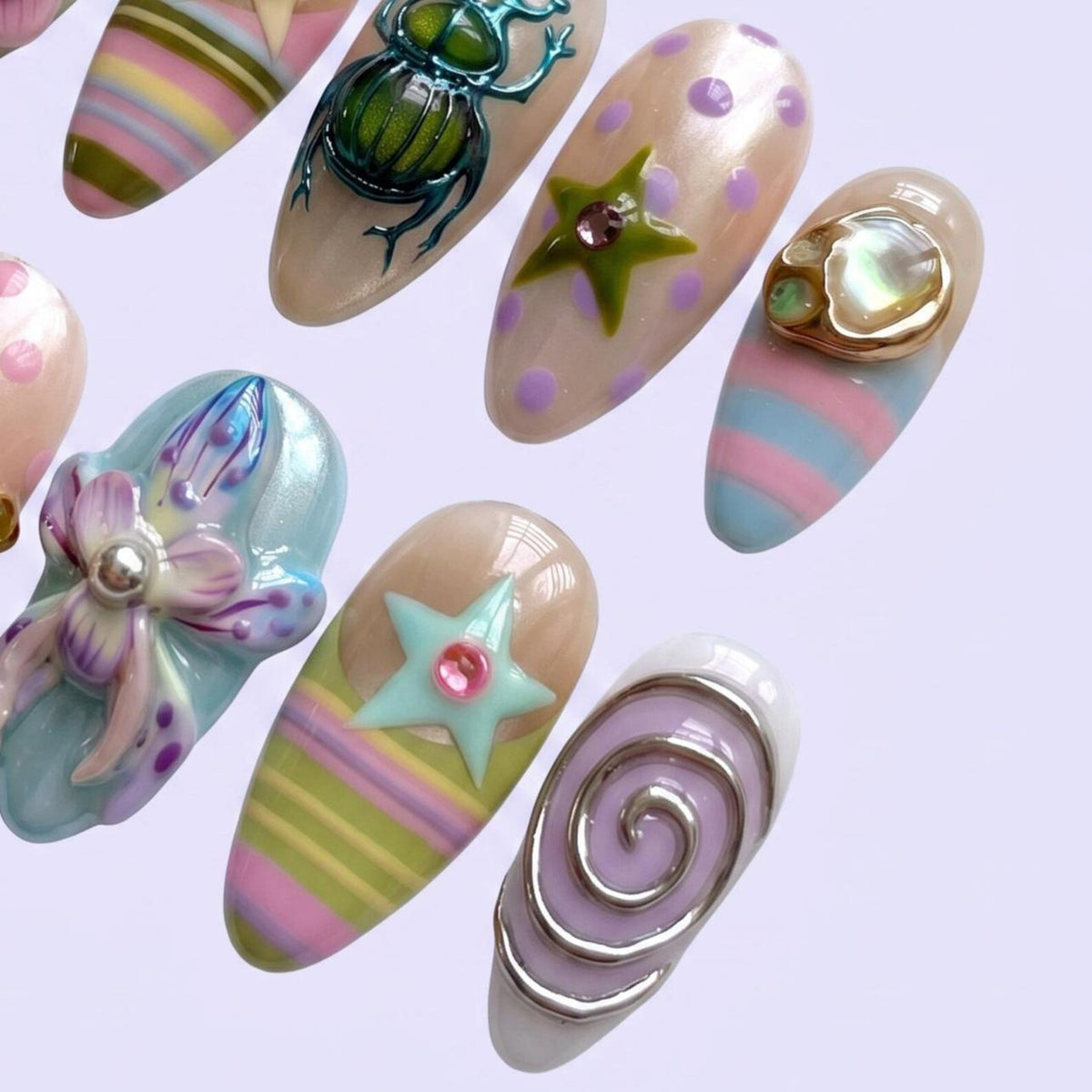 A collection of almond-shaped press-on nails featuring diverse 3D designs including a metallic green beetle, a purple polka-dot nail with a green star, a blue and pink striped nail with a shell accent, a floral motif, and a silver spiral.