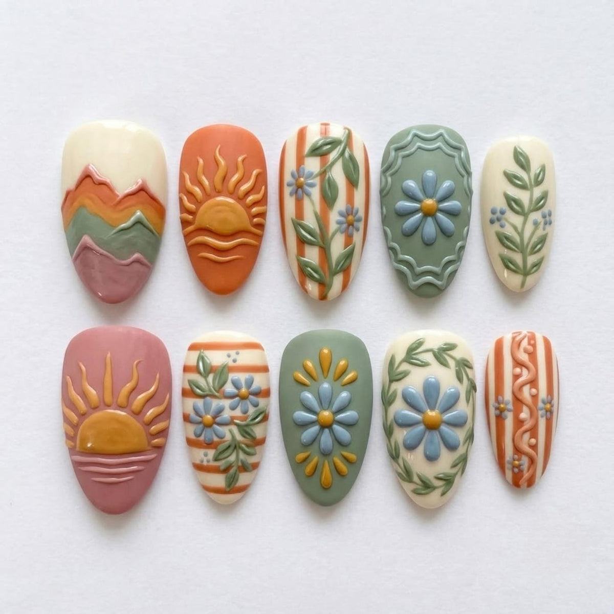 A set of ten almond-shaped press-on nails featuring embossed designs including layered mountain ranges, rising suns over water, vertical stripes with floral vines, daisies within scalloped frames, and intricate botanical patterns in muted tones.