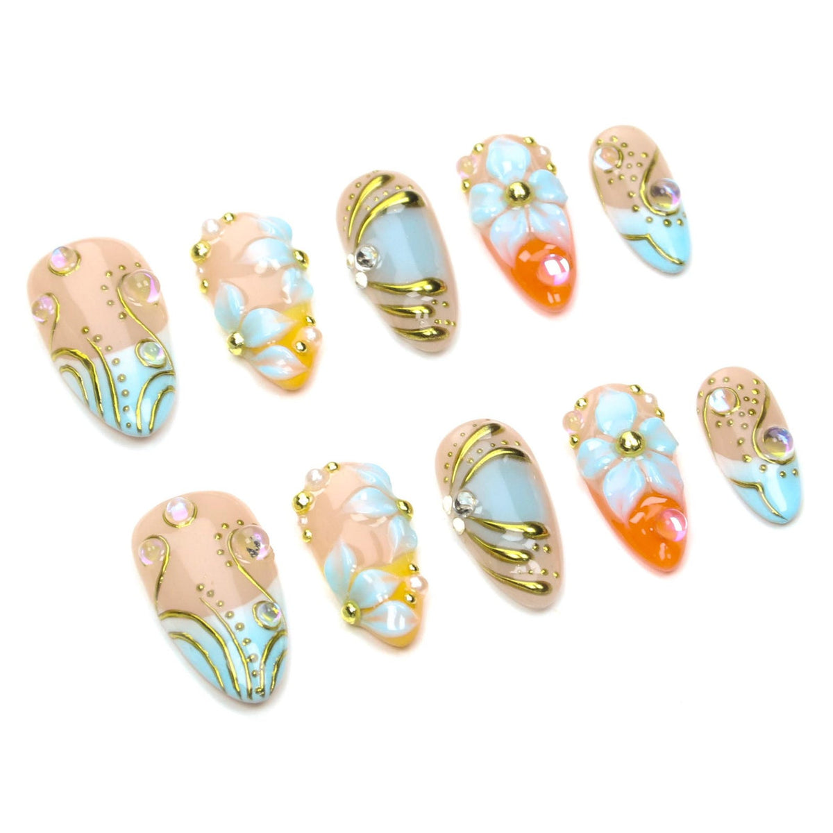 A set of ten almond-shaped press-on nails featuring a nude base with light blue and orange accents. The designs include raised white floral motifs, metallic gold swirling lines, small gold studs, and iridescent rhinestones.