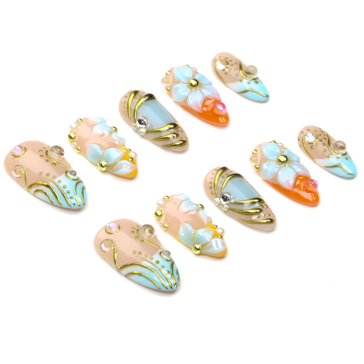 A set of ten almond-shaped press-on nails featuring a nude base with light blue and orange accents. The designs include raised white floral motifs, gold metallic swirls, small gold studs, and iridescent rhinestones on each nail.