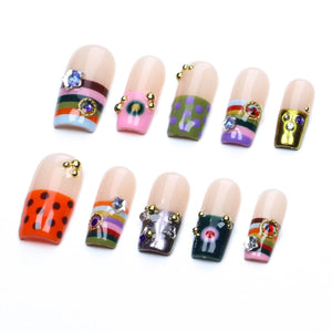 A set of ten press-on artificial nails featuring various designs including horizontal stripes, polka dots, and solid metallic finishes. Each nail is adorned with small gold-toned metal beads and colorful embedded rhinestones.