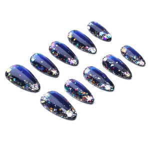 A set of ten almond-shaped press-on nails featuring a deep navy blue base color. Each nail is decorated with a dense gradient of multi-colored metallic foil flakes and fine glitter particles concentrated primarily at the rounded tips.