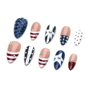 A set of ten almond-shaped press-on nails featuring various designs including navy blue ribbed textures, nude bases with red and white stripes, white stars on navy blue, silver studs, and white nails with red polka dots and metallic accents.