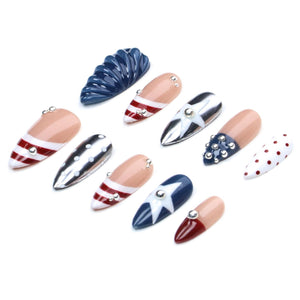 A set of ten press-on nails featuring various designs including red and white stripes, blue with white stars, silver with white polka dots, and solid red or blue accents. Several nails are embellished with small silver metallic studs.