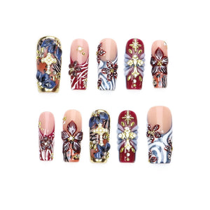 A set of ten press-on nails featuring a variety of designs including deep red, blue, and white patterns, gold cross emblems, floral motifs, and small embedded rhinestones. The nails have a glossy finish and varied rectangular shapes.