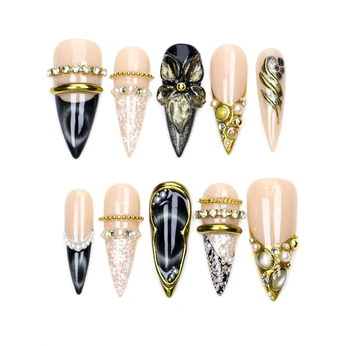A set of ten press-on nails in stiletto and almond shapes, featuring a mix of nude, black, and white colors. The designs include intricate lace patterns, gold metallic bands, clear rhinestones, pearls, and a 3D black floral accent.