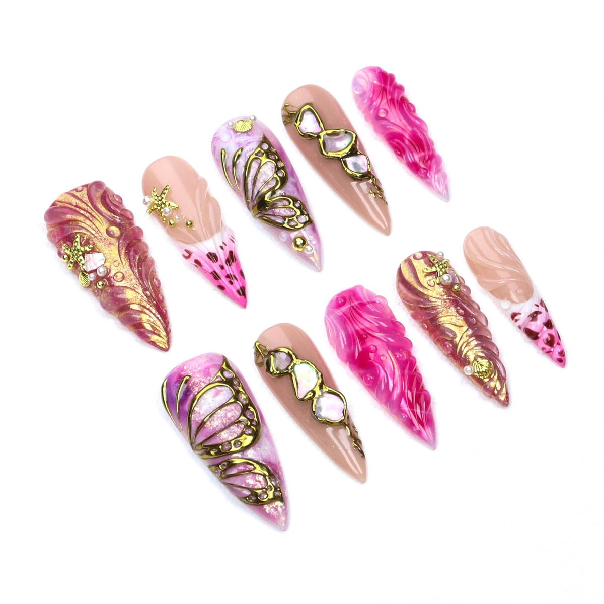 A set of ten stiletto-shaped press-on nails featuring a variety of designs in shades of pink, gold, and nude. The nails are decorated with raised gold butterfly wing patterns, textured swirls, small starfish charms, and embedded rhinestones.