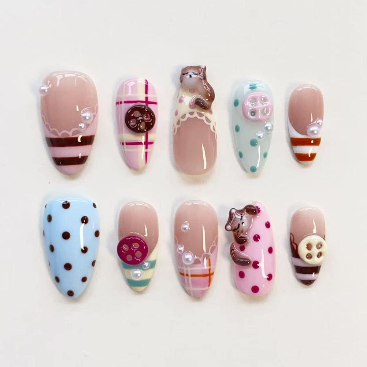 A set of ten press-on nails featuring various designs including pink and blue plaid patterns, polka dots, brown and cream stripes, small white pearls, and three-dimensional sculpted brown bear figures and round buttons.