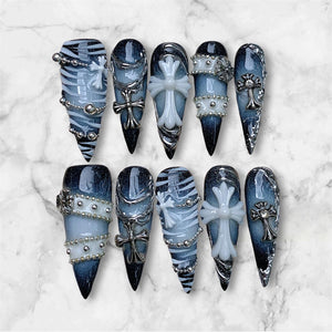 A set of ten stiletto-shaped press-on nails featuring a dark blue and black gradient base. The designs include white zebra stripes, silver metallic chains, small silver studs, and raised white or silver cross emblems on each nail.