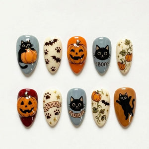 A set of ten almond-shaped press-on nails featuring Halloween designs including black cats, orange pumpkins, bats, paw prints, and vines. The nails are decorated with the text "BOO" on one nail and "TRICK" and "TREAT" on others.