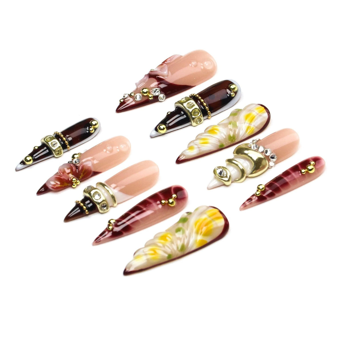 A set of ten stiletto-shaped press-on nails featuring a variety of designs including nude bases, dark burgundy gradients, and floral patterns, accented with gold metallic beads, clear rhinestones, and gold-toned decorative bands.