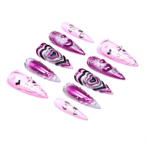 A set of ten stiletto-shaped press-on nails featuring a pink and magenta color palette. The designs include metallic silver accents, raised heart motifs, and black swirling lines, with some nails displaying a glossy finish.