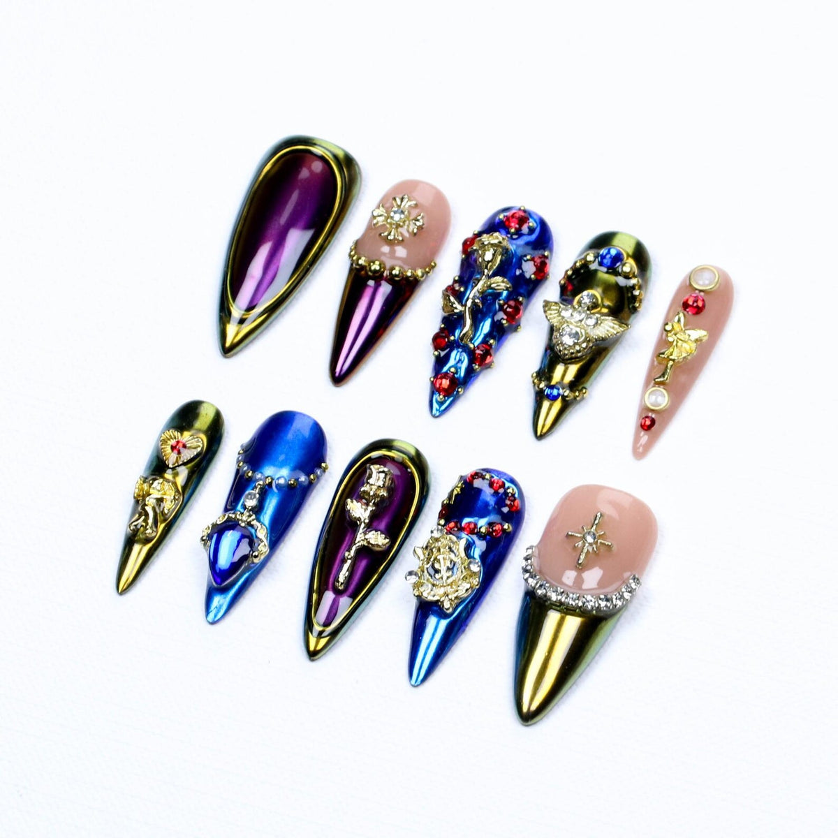 A set of ten stiletto-shaped press-on nails featuring metallic purple, blue, and nude finishes. The nails are decorated with gold-toned charms including roses, crosses, stars, and winged figures, accented with red and clear rhinestones.