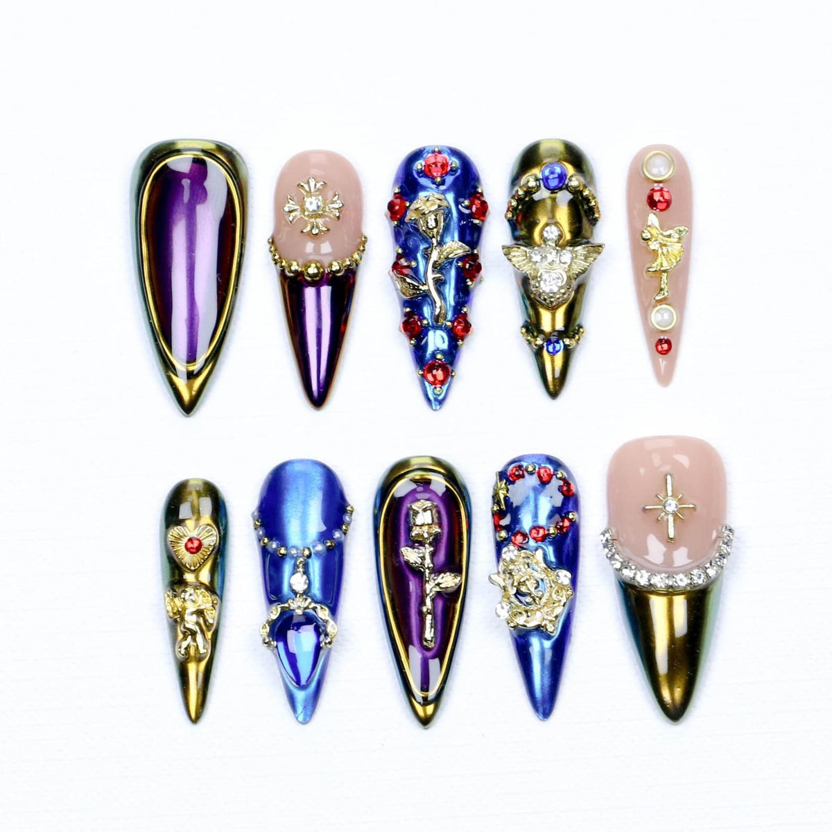 A set of ten stiletto-shaped press-on nails featuring a variety of designs including metallic purple and blue finishes, gold-toned charms like roses, cherubs, and crosses, along with embedded red rhinestones and clear crystals.