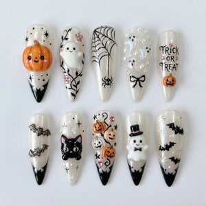 Ten almond-shaped press-on nails with a white shimmer base and black tips. Designs include a 3D orange pumpkin, a white ghost, a black spider web, white pearl ghosts, text reading TRICK OR TREAT, bats, a black cat, and a ghost in a top hat.