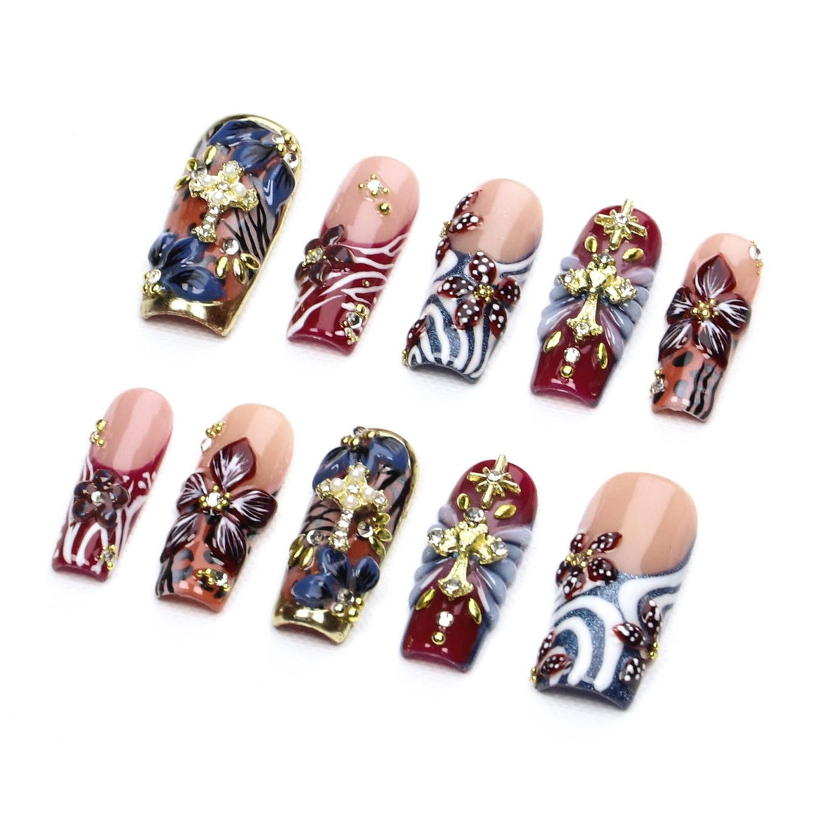 A set of ten press-on nails featuring a variety of designs including deep red, blue, and nude tones. The nails are decorated with three-dimensional floral accents, gold-toned cross charms, and small clear rhinestones.
