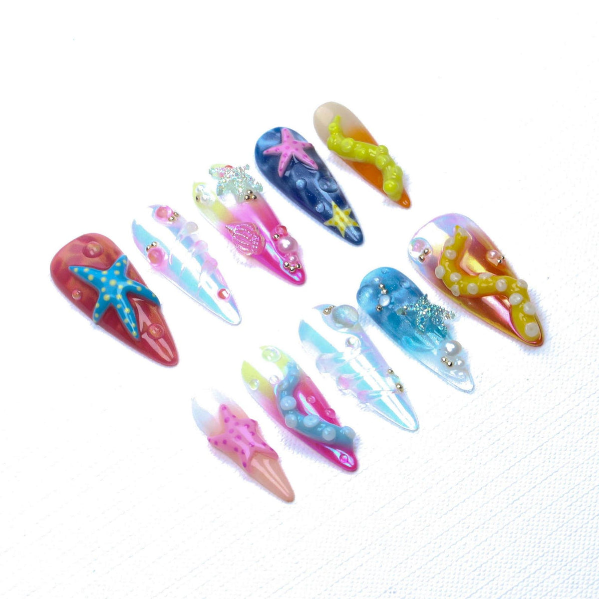 A set of ten press-on nails featuring an ocean theme with vibrant colors, including shades of blue, pink, and yellow. The nails are decorated with three-dimensional starfish, pearl accents, and textured tentacles in various sizes.