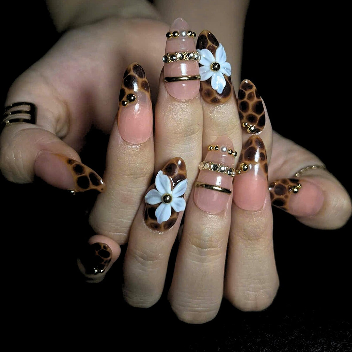 Luxury leopard print press on nails featuring mocha nude tones, tortoise shell accents, 3D white flower, gold embellishments, pearls, and glossy handmade almond nail design.