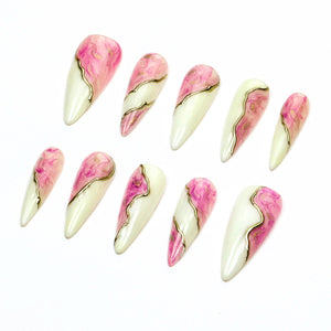 A set of ten almond-shaped press-on nails featuring a split design. Each nail has a creamy off-white base on one side and a swirling pink and white marble pattern on the other, separated by a thin, raised metallic gold line.
