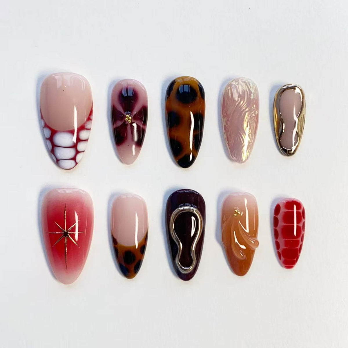 A set of ten almond-shaped press-on nails featuring diverse designs including white and red reptile textures, leopard print, metallic gold accents, a red starburst pattern, and glossy solid colors in shades of red, brown, and nude.