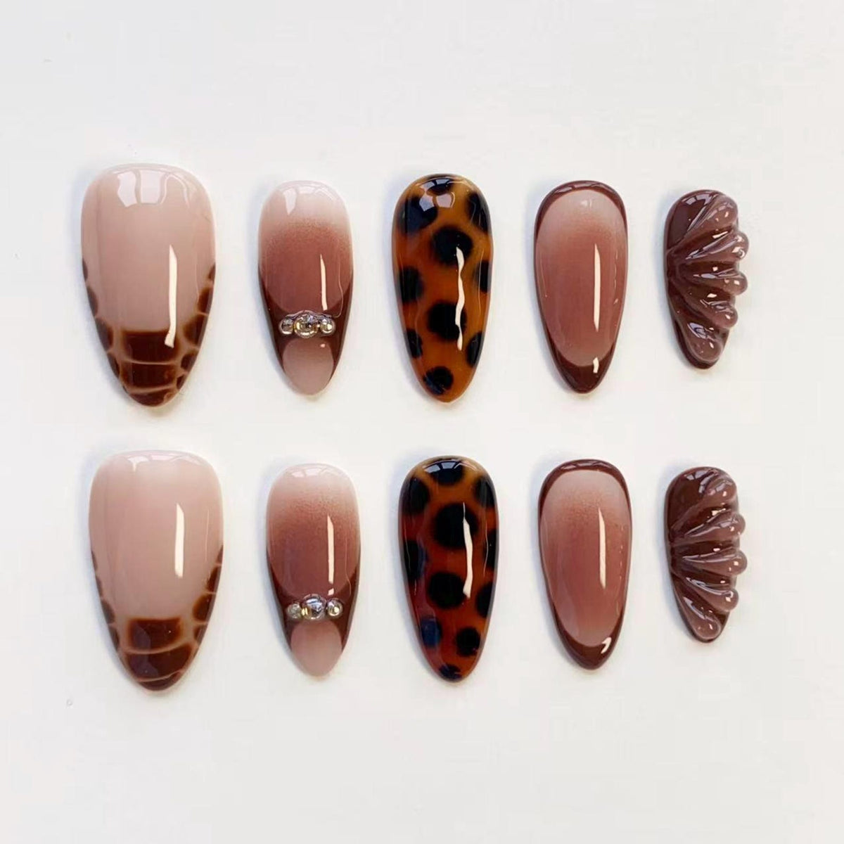 A set of ten press-on nails featuring various designs including brown and nude ombre, leopard print, dark brown French tips, and textured 3D shell-like patterns. Some nails are accented with small clear rhinestones near the cuticle area.