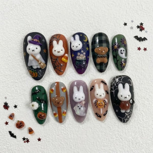 A set of ten almond-shaped press-on nails featuring Halloween-themed designs. The nails display 3D white rabbit figures, pumpkins, ghosts, a teddy bear, candy corn, spider webs, and bats in a color palette of black, orange, green, and purple.