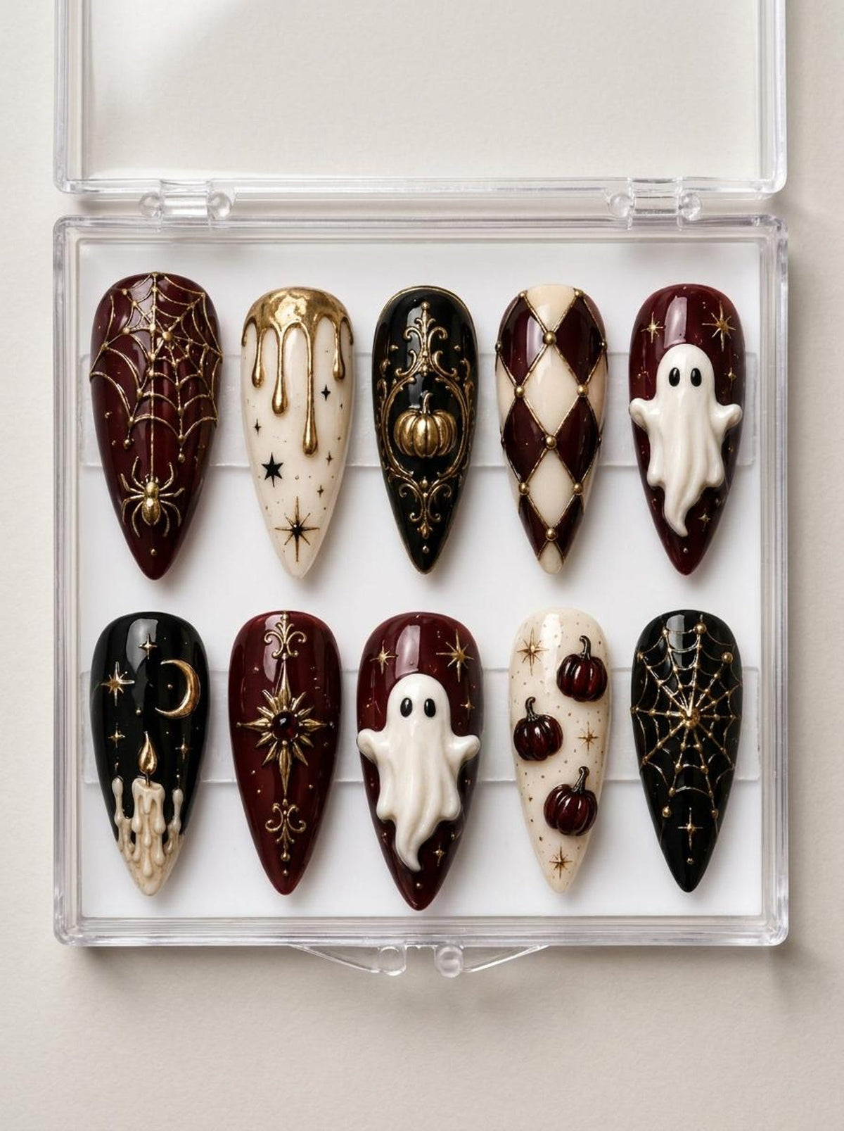 A set of ten almond-shaped press-on nails in a clear plastic case, featuring Halloween-themed designs in black, cream, and deep red with gold accents, including raised 3D ghosts, pumpkins, spiderwebs, stars, and candle motifs.