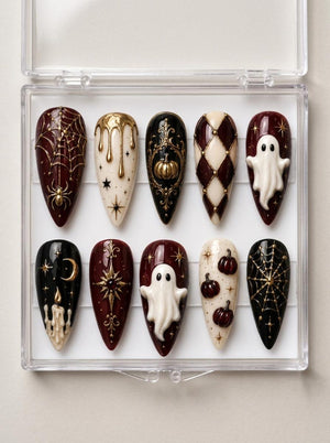 A set of ten almond-shaped press-on nails in a clear plastic case, featuring Halloween-themed designs in black, cream, and deep red with gold accents, including raised 3D ghosts, pumpkins, spiderwebs, stars, and candle motifs.
