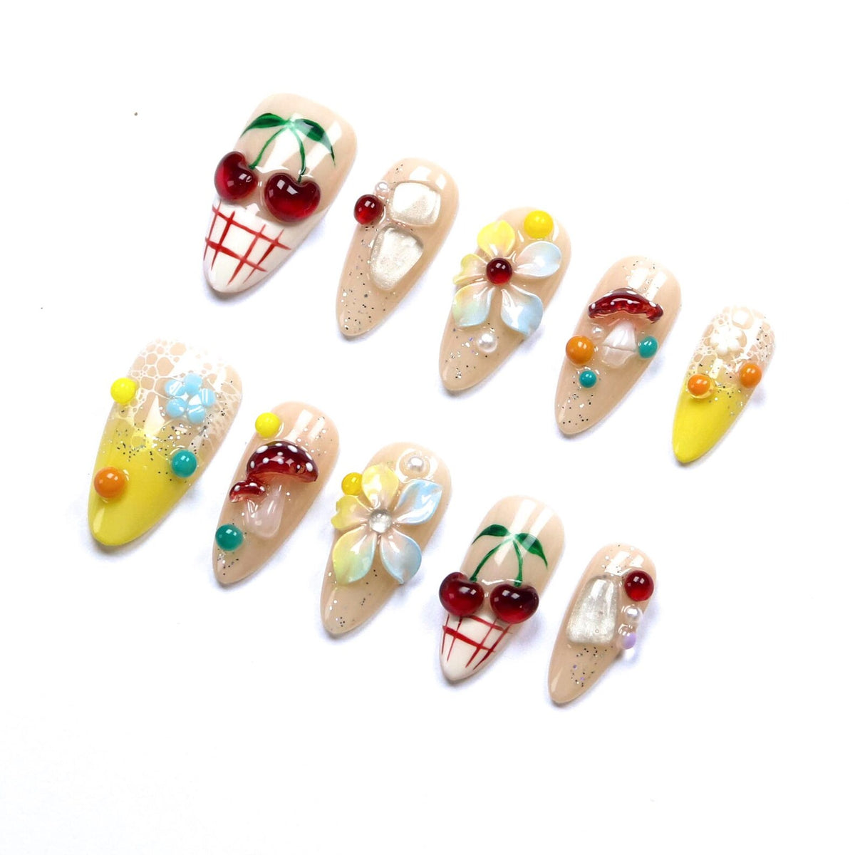 A set of ten press-on nails featuring a nude base with various 3D embellishments including red cherries, colorful flowers, mushrooms, and small beads. Some nails have a yellow gradient, white grid patterns, and glitter accents.