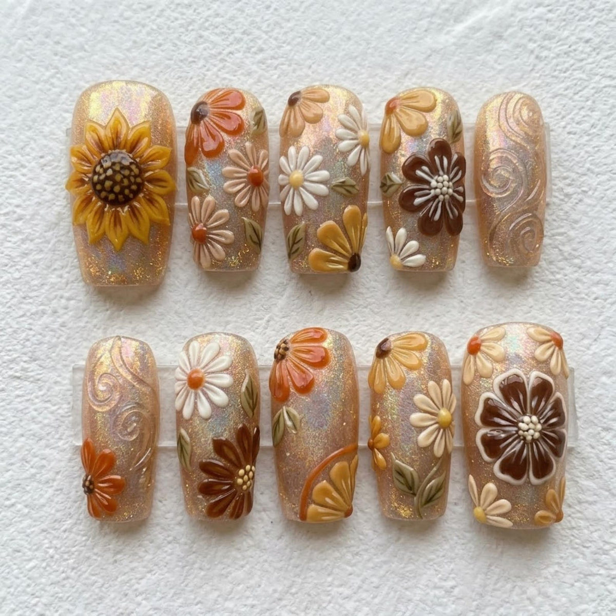 A set of ten press-on nails featuring a shimmering, iridescent beige base. The designs include raised 3D floral motifs in shades of yellow, orange, brown, and white, alongside delicate embossed swirl patterns on select nail tips.