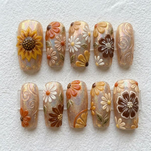A set of ten press-on nails featuring a shimmering, iridescent beige base. The designs include raised 3D floral motifs in shades of yellow, orange, brown, and white, alongside delicate embossed swirl patterns on select nail tips.