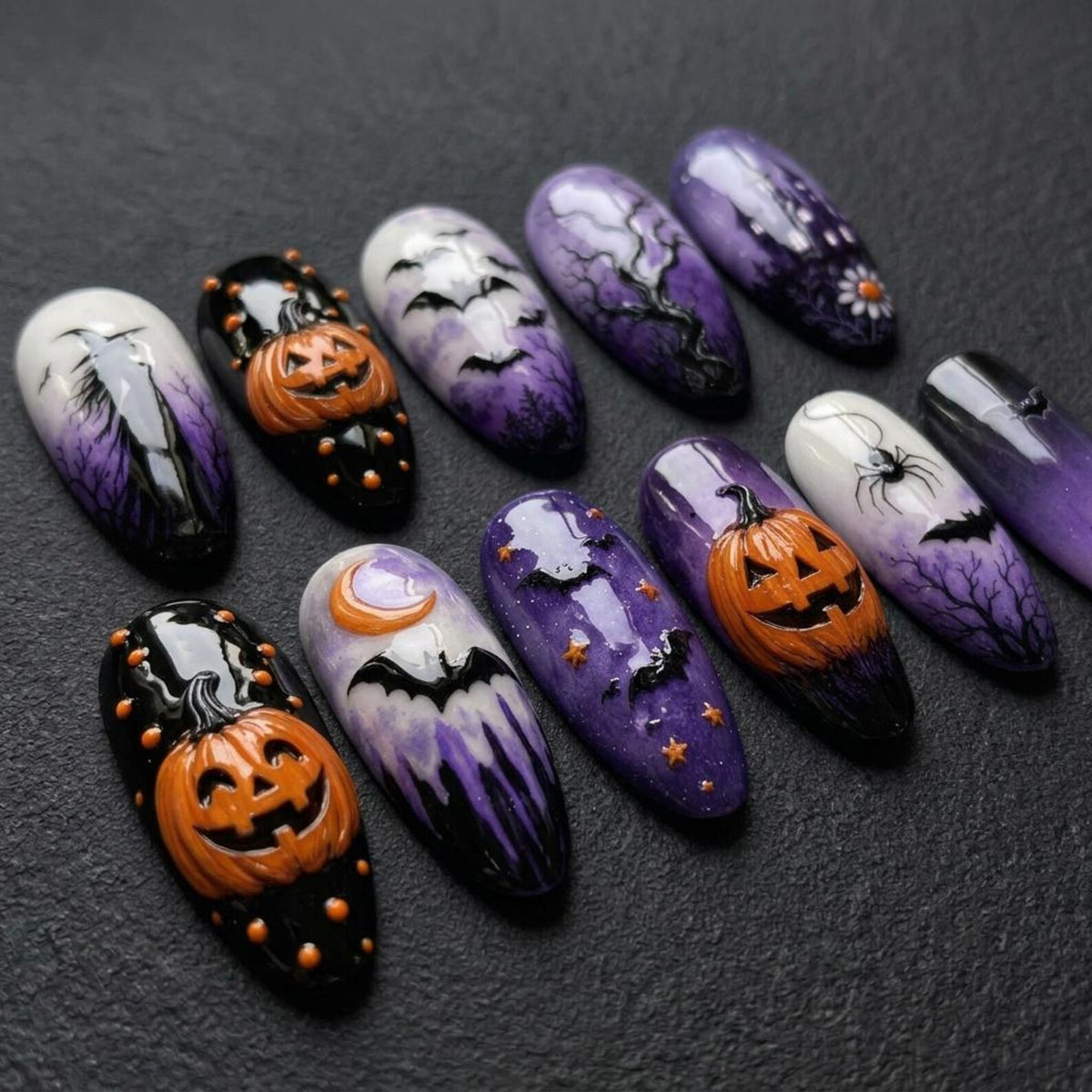 A set of ten almond-shaped press-on nails featuring Halloween designs. The nails display orange pumpkins, black bats, purple and white gradient backgrounds, silhouettes of trees, a crescent moon, stars, and a black spider.