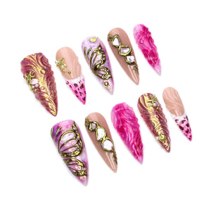 A set of ten stiletto-shaped press-on nails featuring a variety of designs including pink and gold marbled patterns, gold butterfly wing motifs, white shell-like accents, small gold starfish charms, and pink leopard print tips.