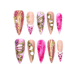 A set of ten stiletto-shaped press-on nails featuring pink and gold color palettes. Designs include raised gold butterfly wings, textured swirls, metallic accents, and small starfish embellishments on a glossy, multi-tonal pink base.
