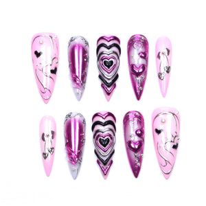 A set of ten stiletto-shaped press-on nails in shades of pink, magenta, and black. The designs feature metallic chrome finishes, raised 3D heart motifs, silver line art, and small embedded rhinestones on a glossy, smooth surface.