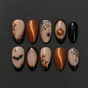 A set of ten press-on nails featuring a Halloween theme with a nude base. Designs include metallic gold leaves, shimmering copper, black spiderwebs with spiders, a pumpkin in a gold frame, a black bat, and small gold stars.