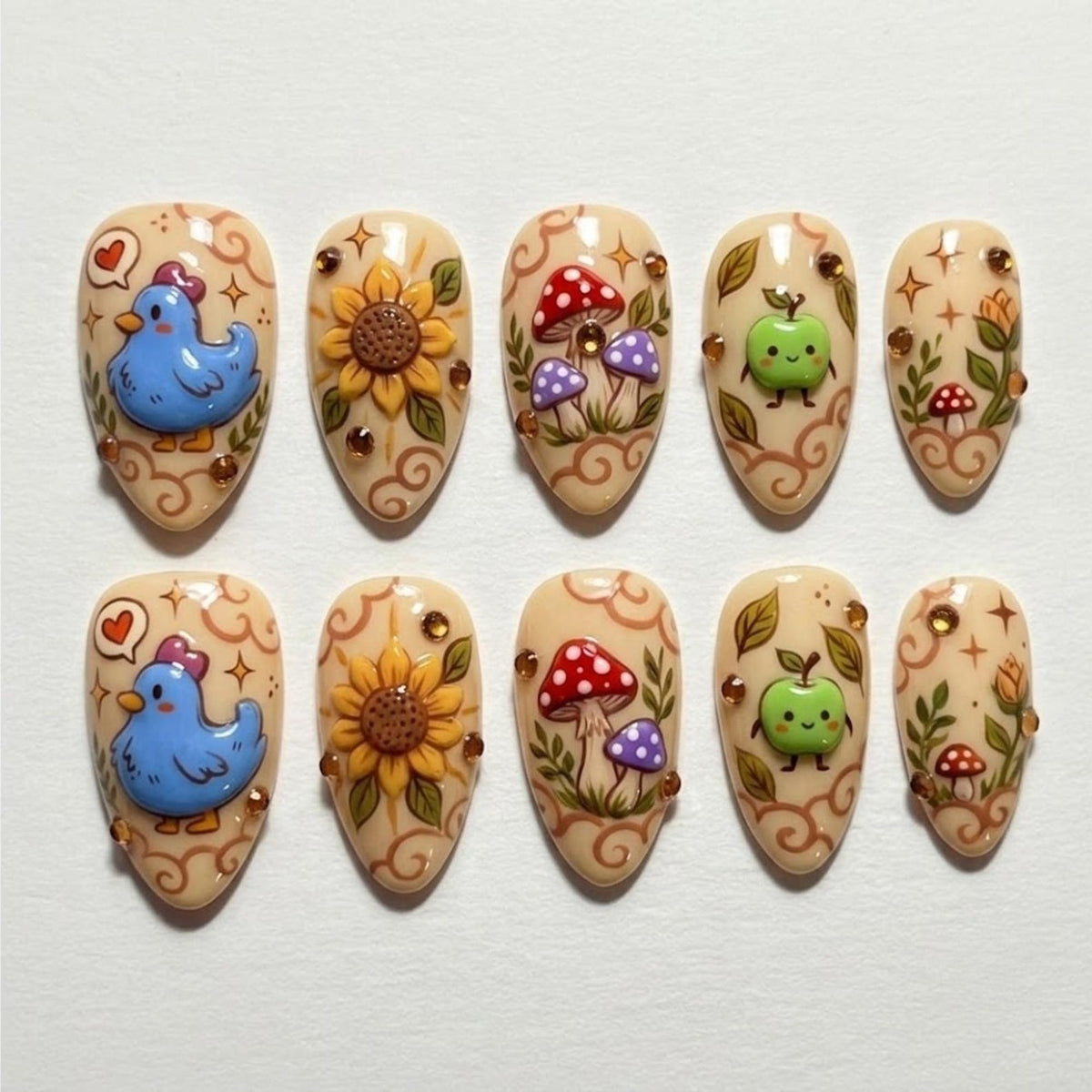 A set of ten almond-shaped press-on nails with a cream base, featuring hand-painted designs of blue birds, yellow sunflowers, red and purple mushrooms, green apples, and foliage, accented with small brown rhinestones and star motifs.