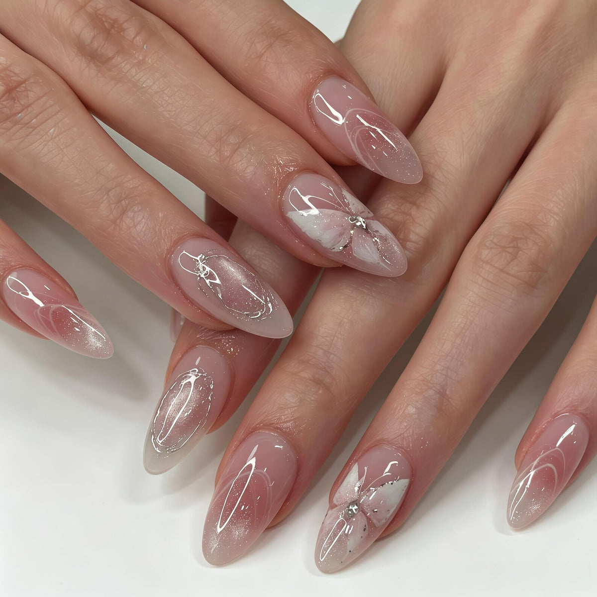 Almond-shaped nails featuring a sheer nude base with delicate white painted butterfly wing designs, silver glitter accents, and thin white line detailing. The manicure includes subtle shimmer and small clear rhinestones.