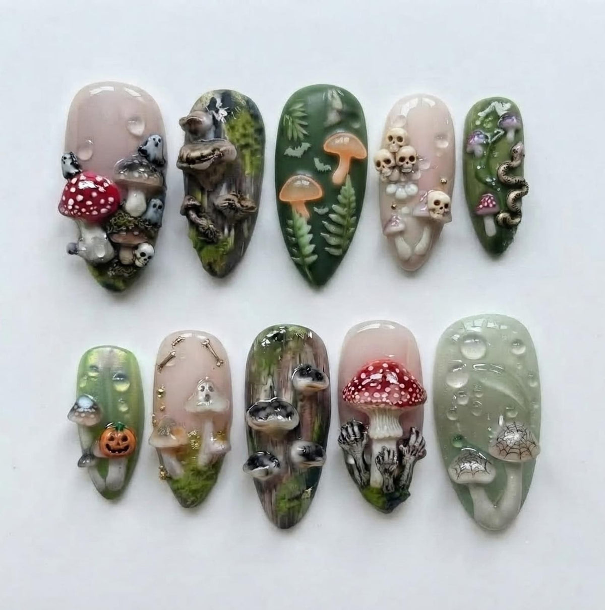 A set of ten press-on nails featuring 3D designs including mushrooms, skulls, ghosts, a jack-o'-lantern, snakes, and spiderwebs. The color palette includes shades of green, cream, white, and red with glossy finishes and water droplets.