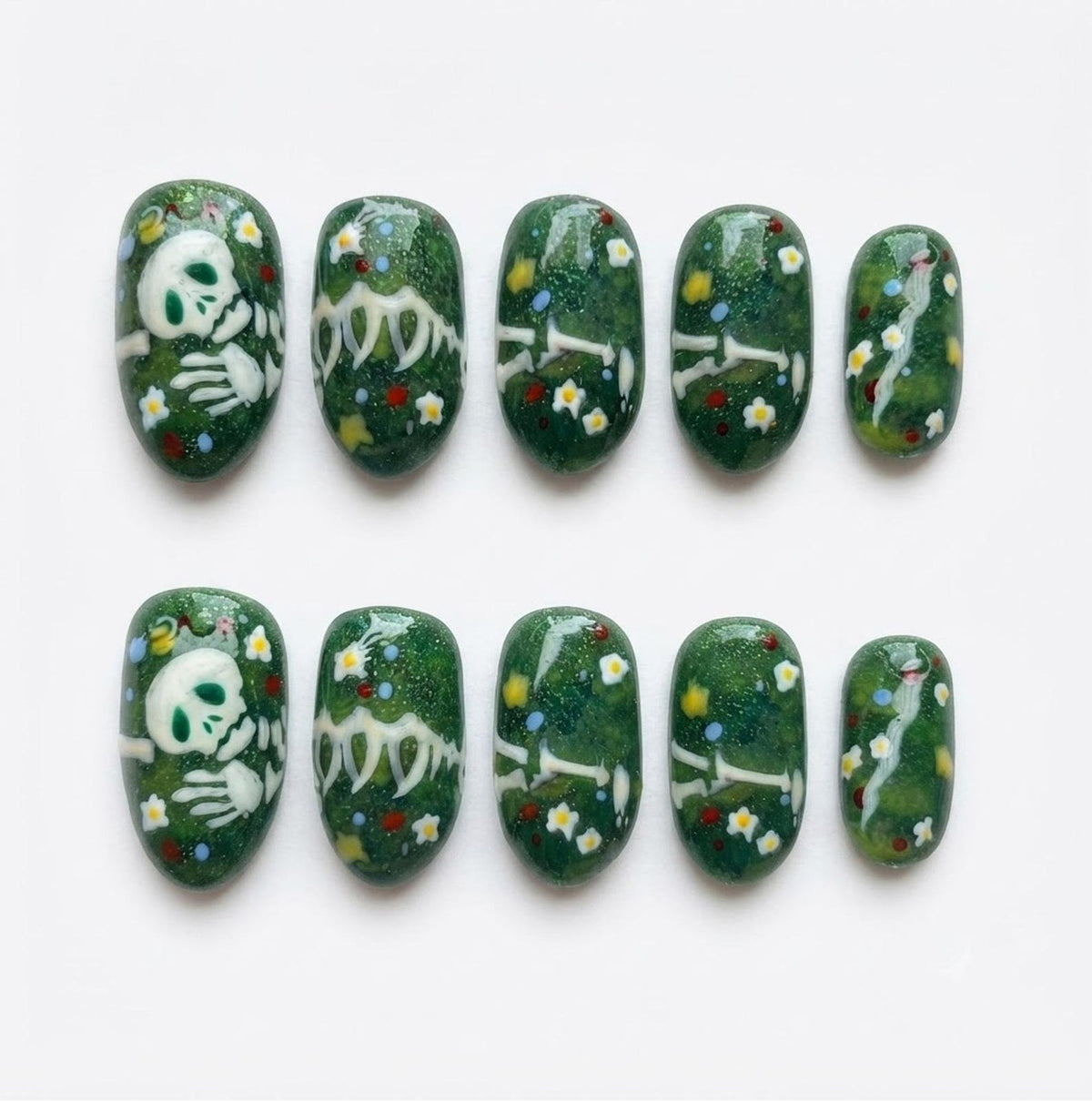 A set of ten press-on nails featuring a dark green base with a glittery finish. The design includes white skeletal hand and arm bones, small white and yellow flowers, and tiny red and blue dots scattered across the surface of each nail.